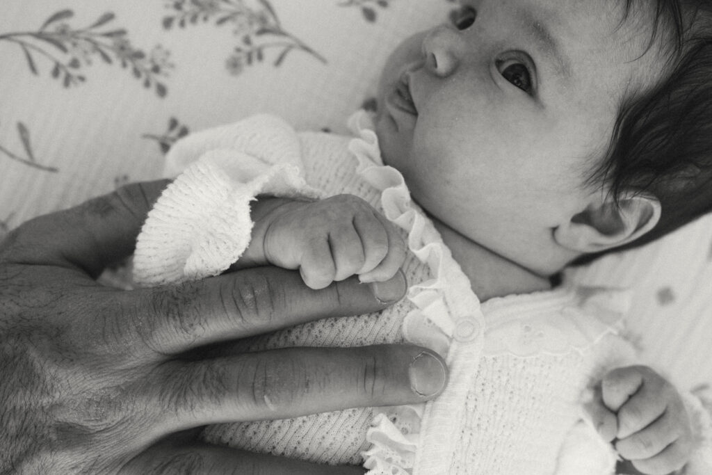 black and white photo of baby holding dad's hand